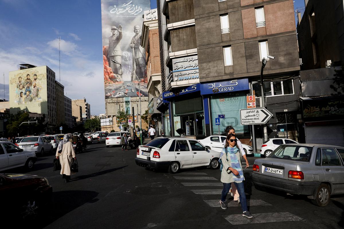 People walk past a billboard about the Strait of Hormuz in Tehran, Iran, on Sunday. Iran’s leaders are splashing propaganda posters across Tehran boasting of national unity and victory over a global superpower.