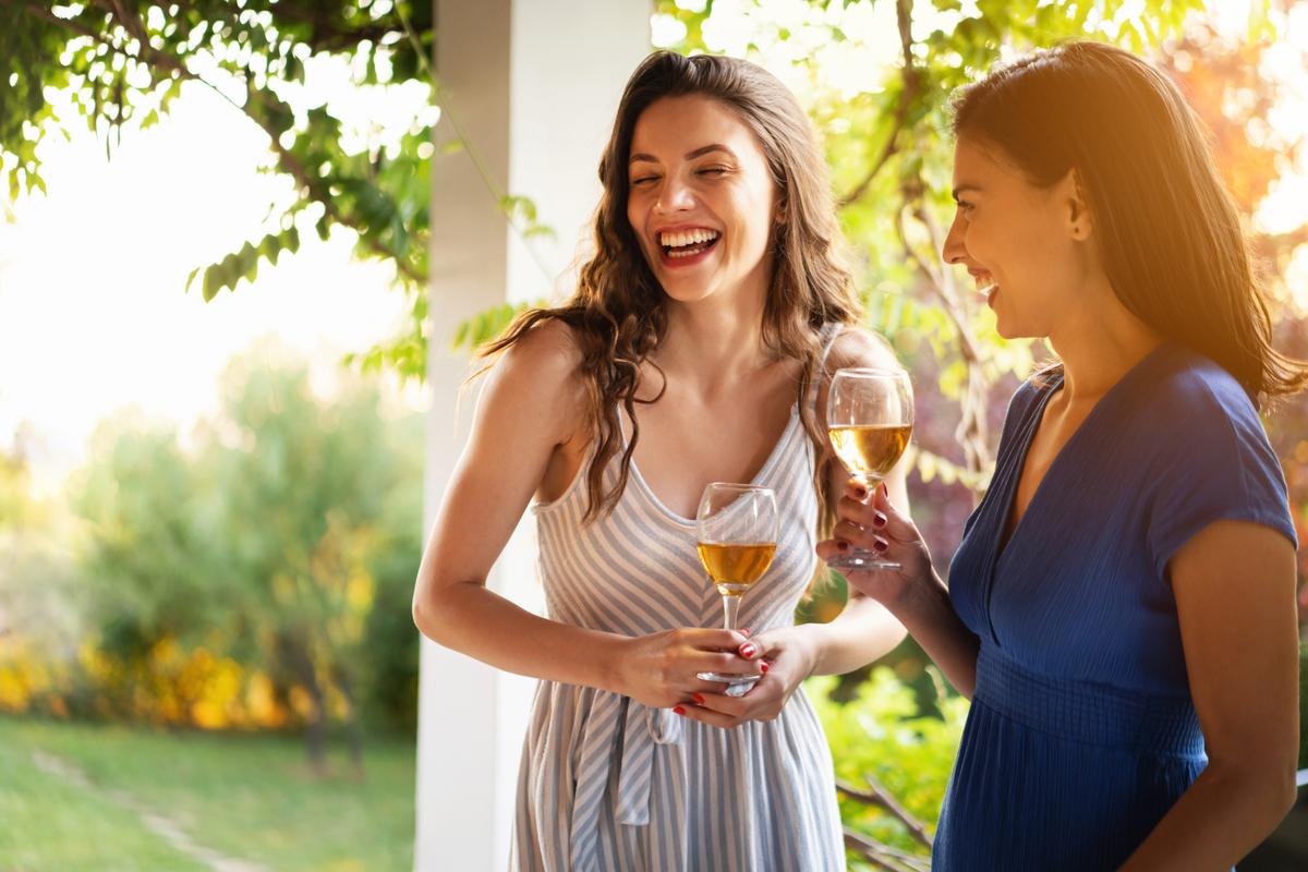 Friends drinking wine while having a casual conversation during summer garden party.