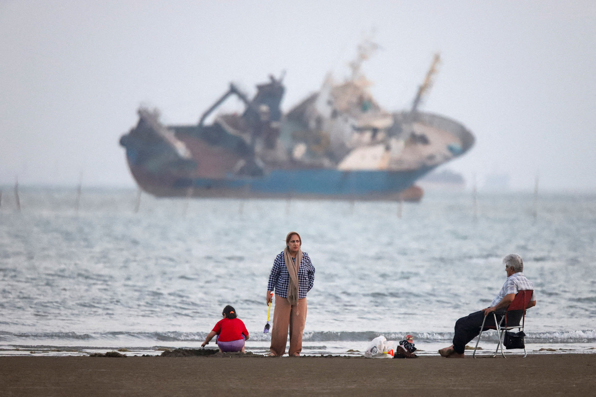 People gather on a beach, as a vessel in the Strait of Hormuz is visible, near the beach of Bandar Abbas, Iran, May 31, 2026.