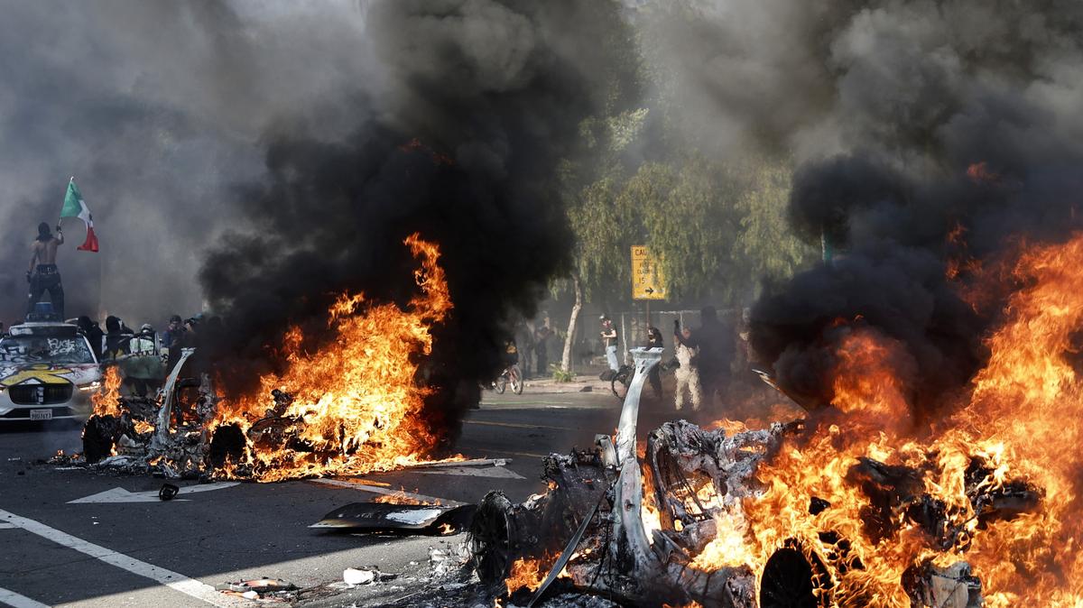 Los Angeles protesters riots. A protester holds up a Mexican flag as burning Waymo cars line the street on June 8, 2025 in Los Angeles, California.