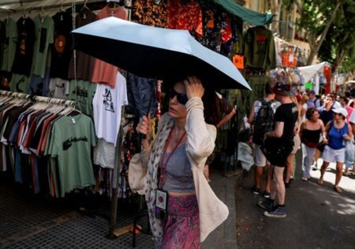 A woman walks with an umbrella, as tourists and residents shop at El Rastro flea market during a hot summer day in central Madrid, Spain June 21, 2026.  REUTERS/Mohammed Salem